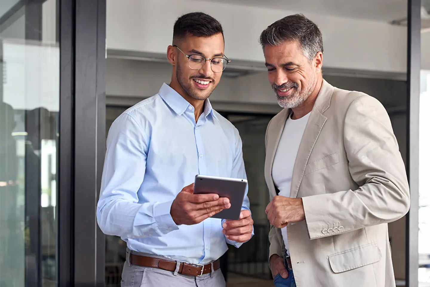 Zwei gut gelaunte Geschäftsleute arbeiten in einem Büro zusammen. Sie stehen und verwenden ein digitales Tablet.