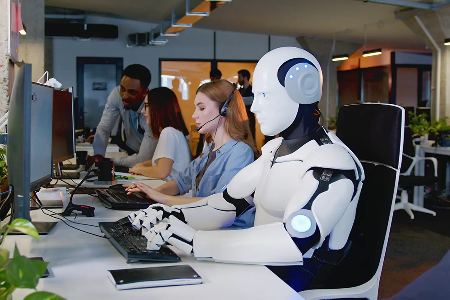 Robot working in an office at computer among people